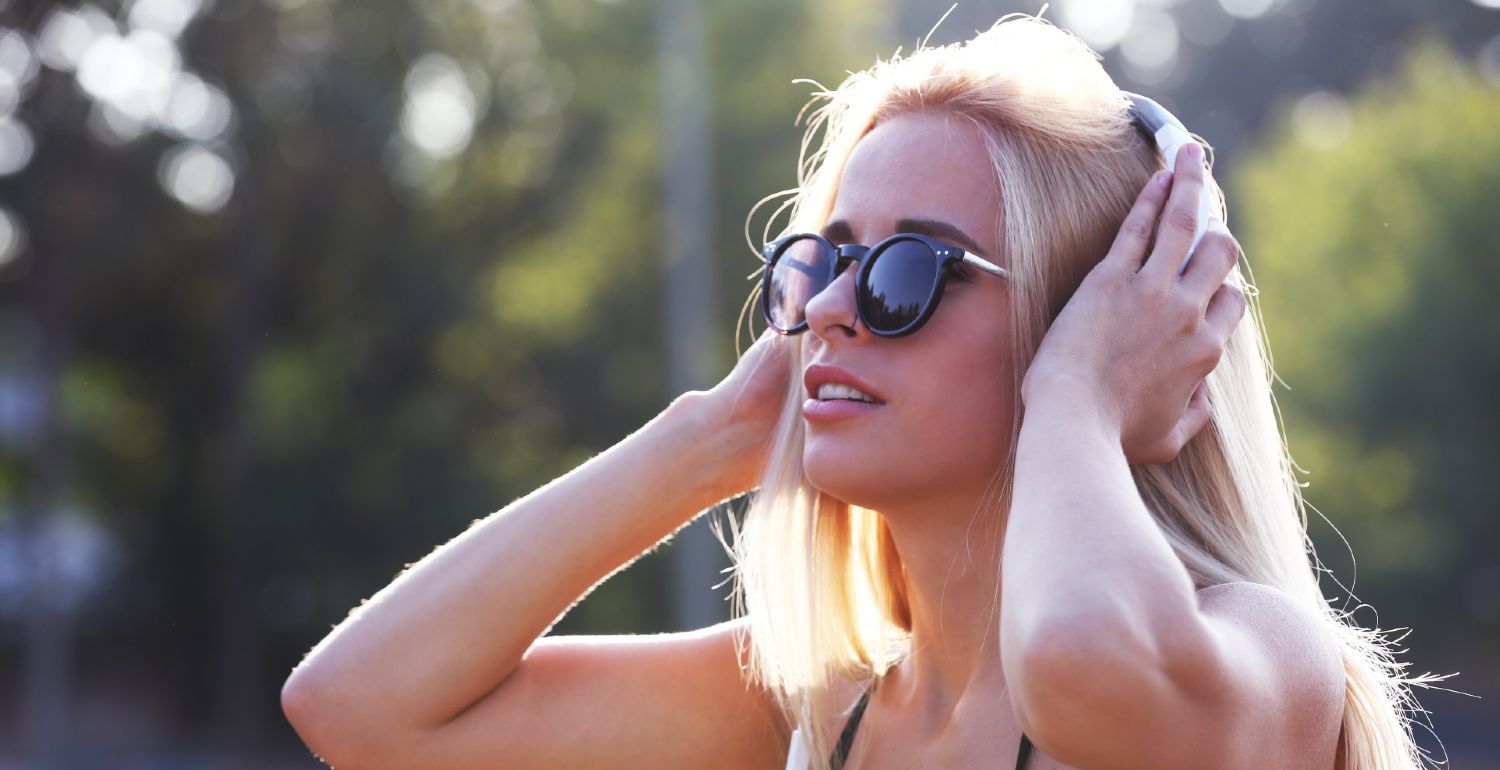 Kvinde med solbriller lytter til musik på sin mobil udendørs