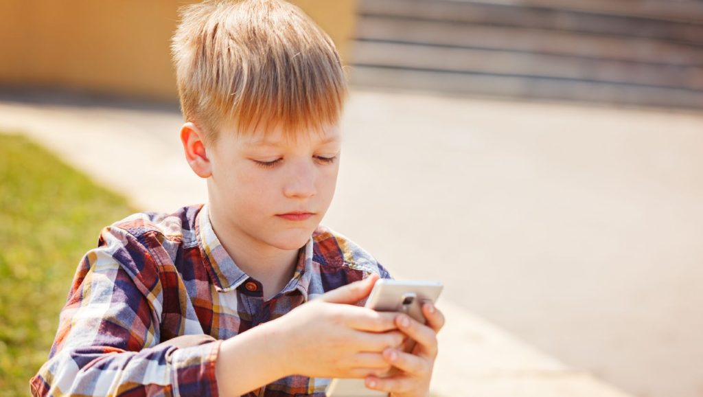 Dreng i ternet skjorte bruger sin mobiltelefon udenfor