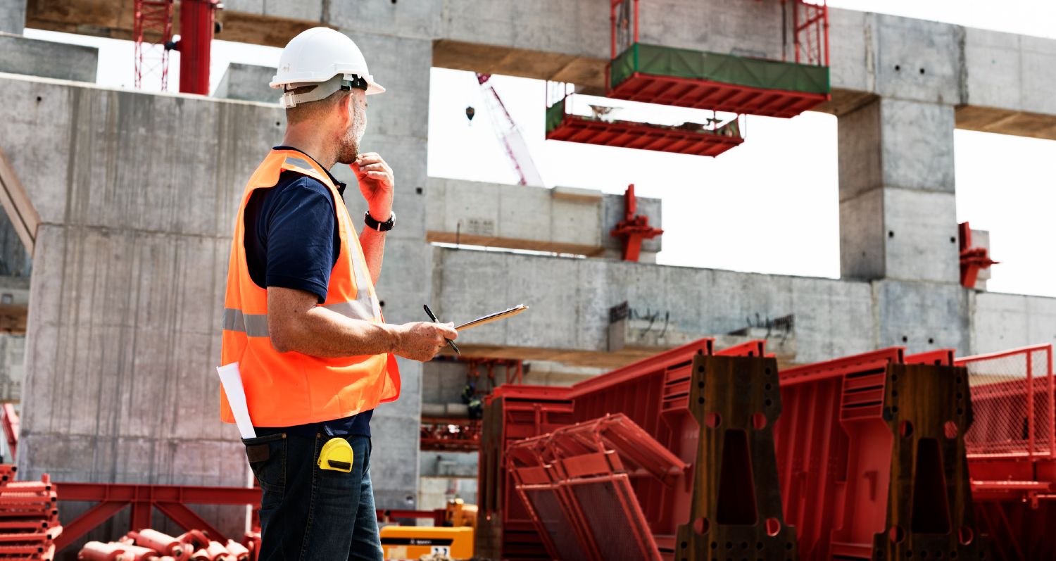 Arbejder i orange refleksvest observerer en byggeplads ved stor betonkonstruktion