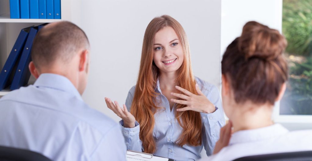 Kvinde i blå skjorte til jobsamtale i kontorlokale med mandlig og kvindelig leder