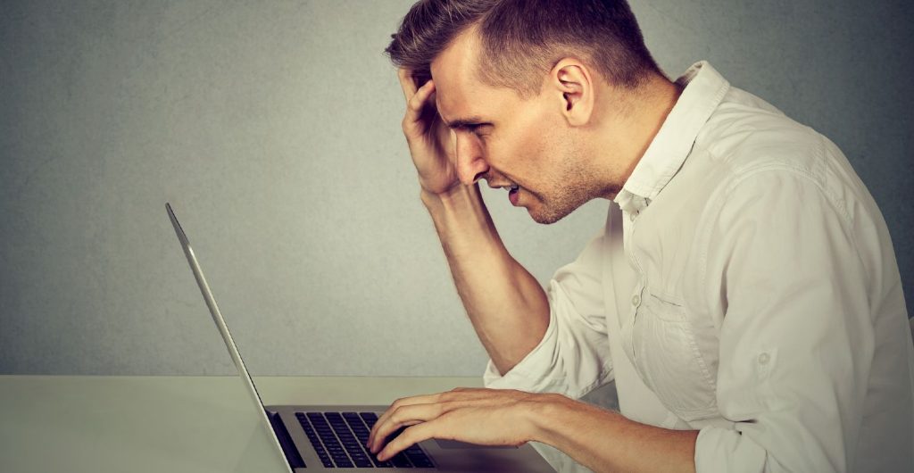Mand i hvid skjorte med laptop frustreret over langsomt internet
